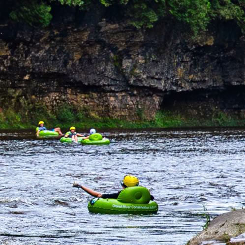 People sitting in green tubes floating down the Grand River.