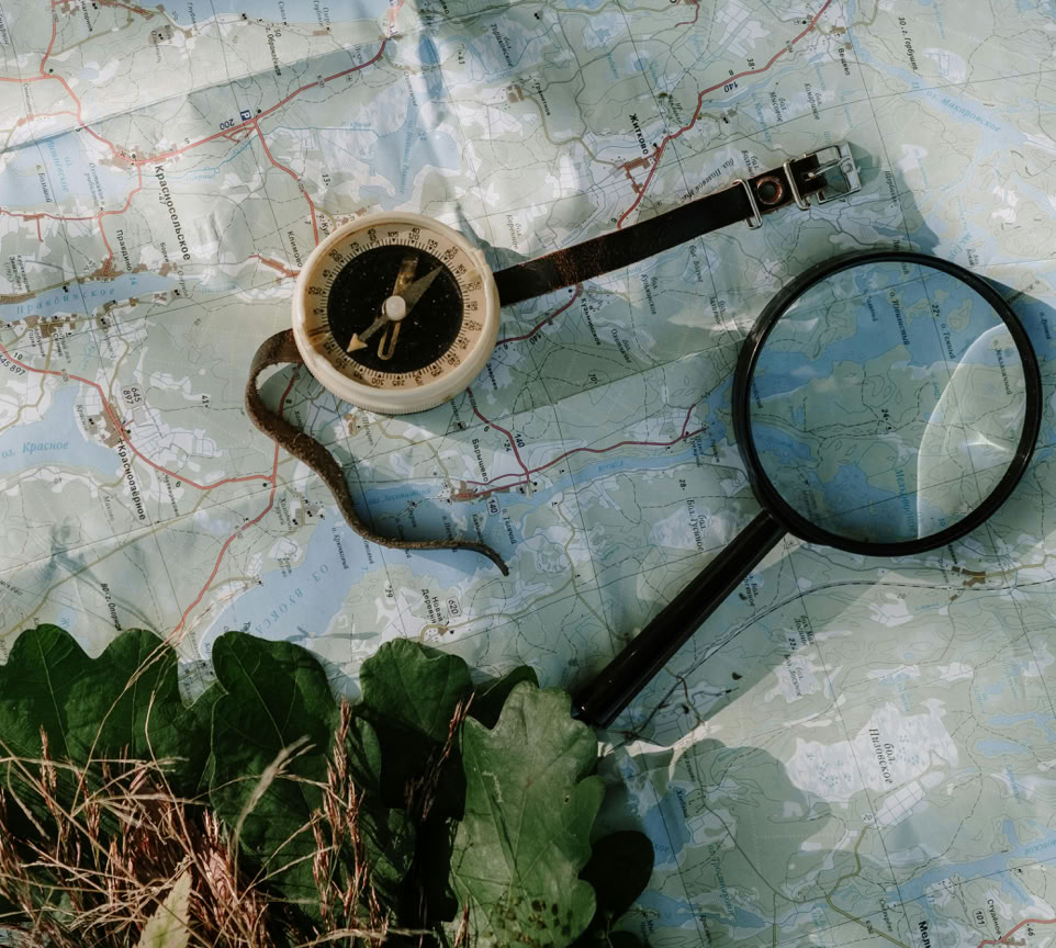 A compass and magnifying glass on a map with leaves. Perfect for travel or exploration themes.