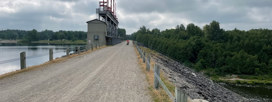 A scenic view of the road crossing the Shand Dam at Lake Belwood with cyclist in the distance