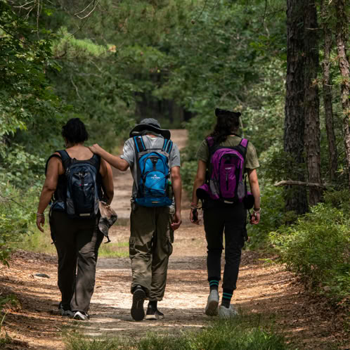 Three friends wearing backpacks walking along trail 
