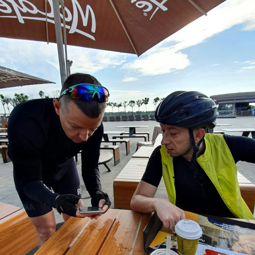 Two cyclists looking at cell phone on a cafe table with take out coffee cup in foreground