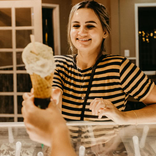 Woman at ice cream counter admiring an ice cream waffle cone with a couple of scoops 