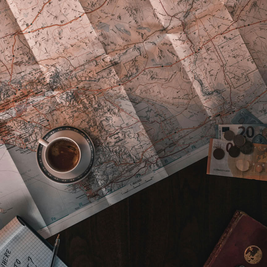 Flat lay of map, coffee, coins, and notebook for travel planning.