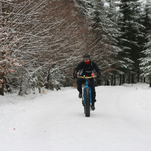 Man peddling a bike on a snow covered trail.