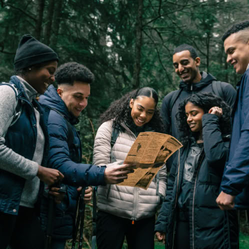 Six people gathered together looking at a map in the woods